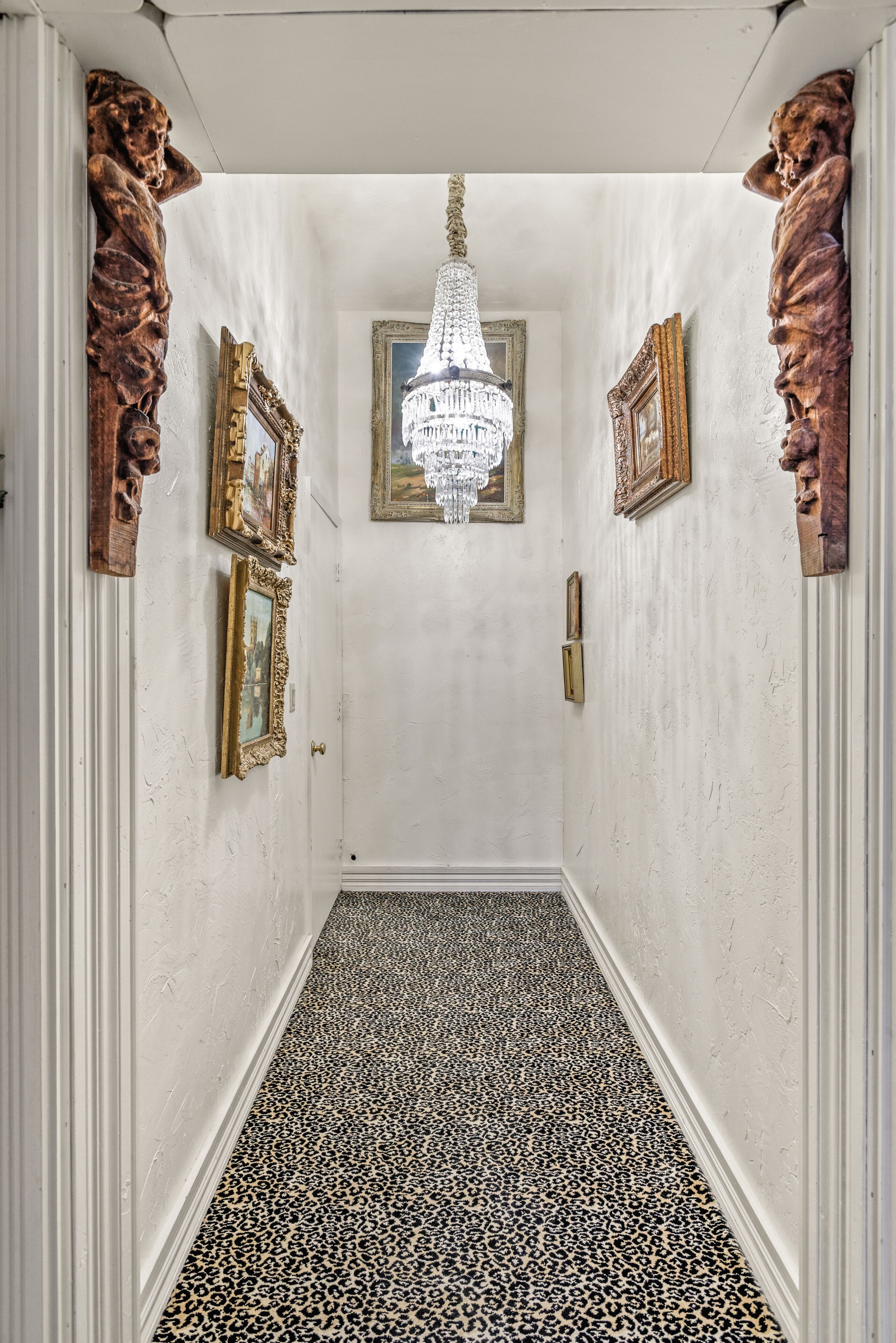 A hallway with a chandelier, framed pictures, and a leopard print floor.