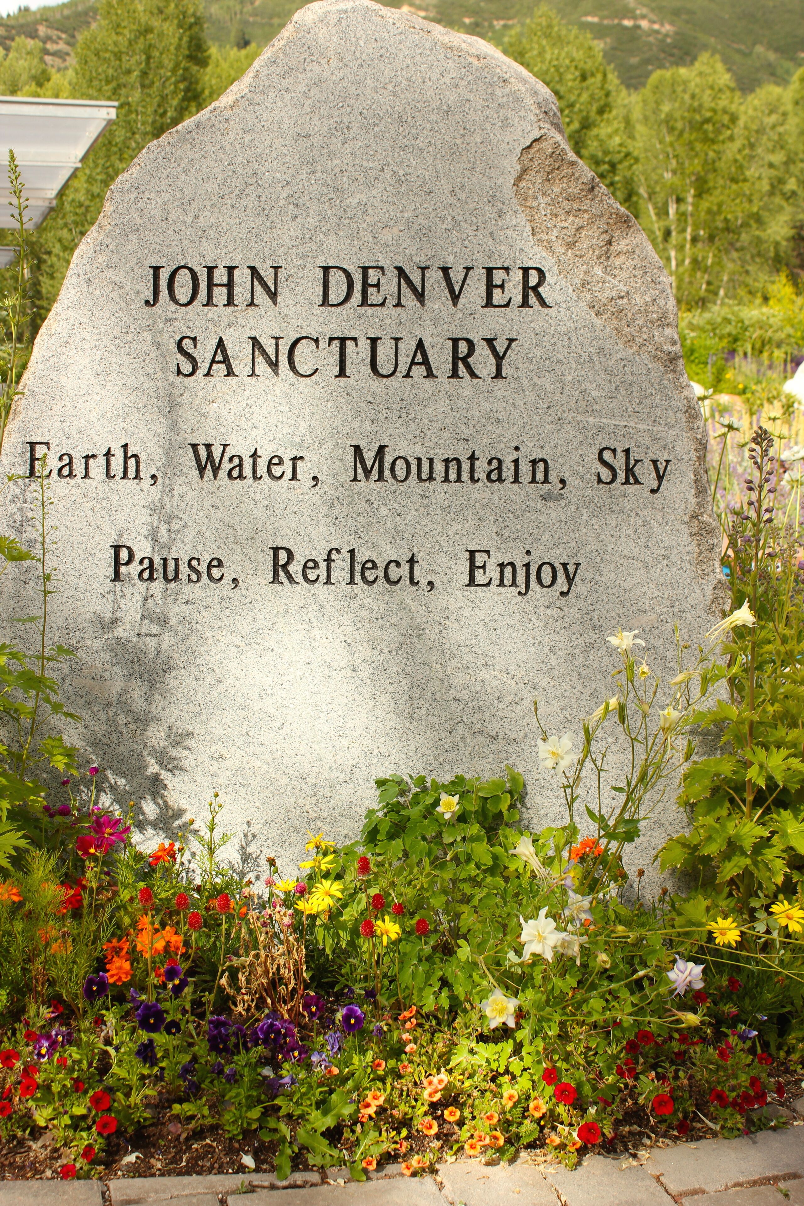 Une plaque de pierre portant l’inscription « Sanctuaire John Denver » et une liste de mots en dessous.