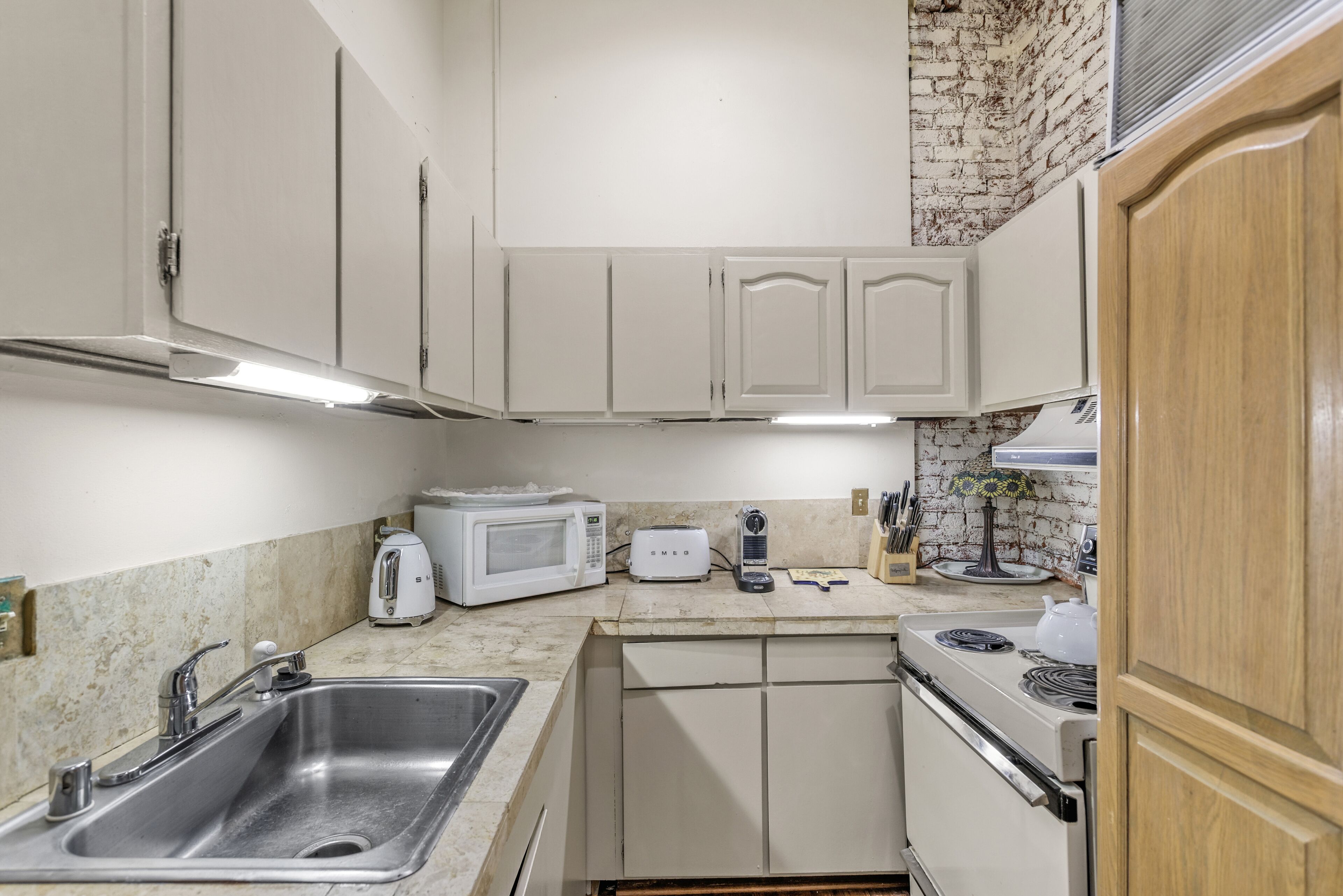 A compact kitchen with white cabinets, a stainless steel sink, a microwave, a toaster, and a stove.