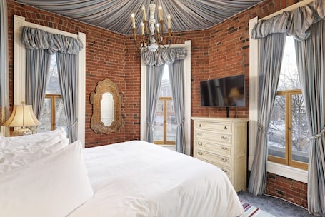 A bedroom with a large bed, a dresser, a TV, and a chandelier.