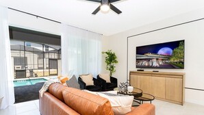 Ein modernes Wohnzimmer mit einer Ledersofa, einem schwarzen Sessel, einem Glastisch und einem an der Wand befestigten Fernseher.