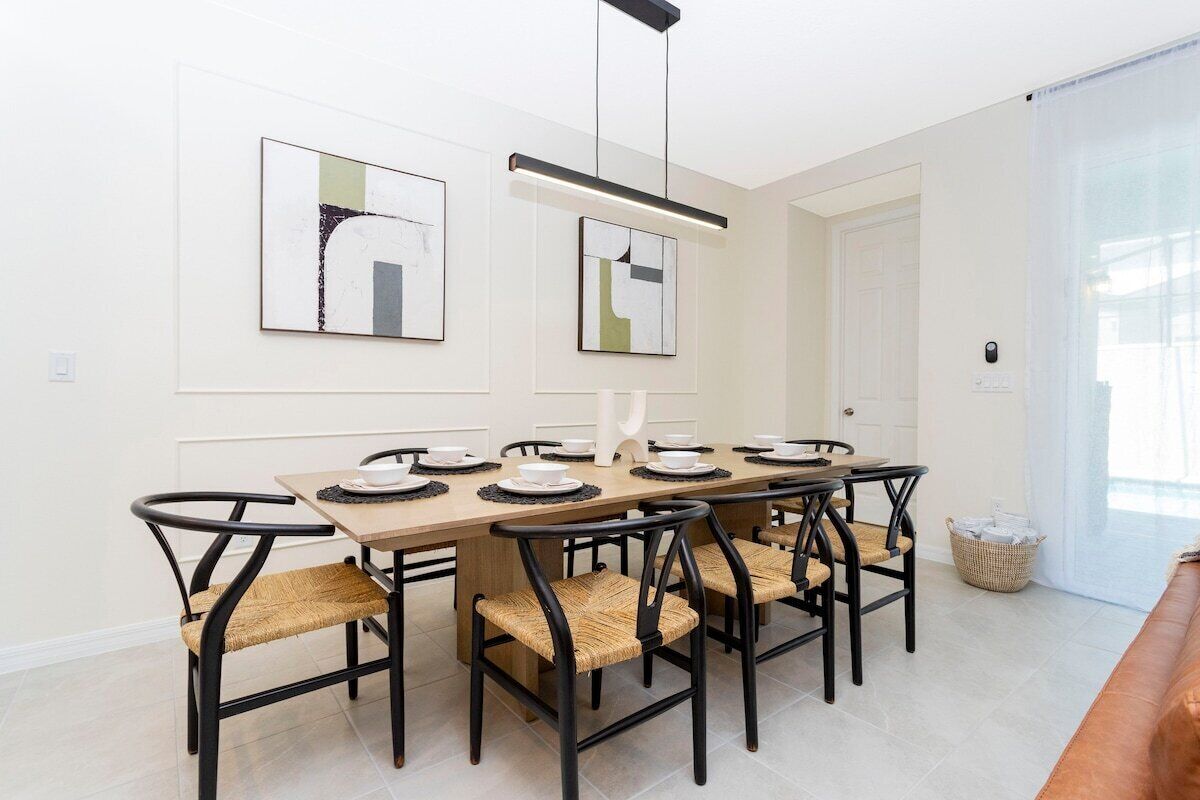 A dining area with a long wooden table, black chairs with woven seats, and abstract artwork on the walls.