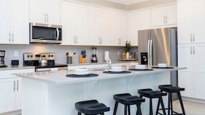 Eine moderne Küche mit weißen Schränken, einem Edelstahl-Kühlschrank, einer Mikrowelle, einem Herd und einer großen Kochinsel mit Barhocker.