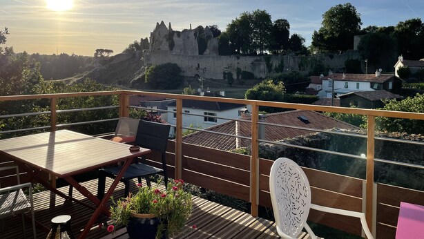 Un balcón con mesa y sillas, con vistas a un castillo histórico y un río.