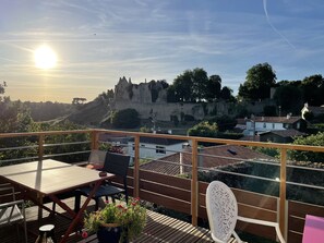 A balcony with a table and chairs, overlooking a historic castle and a river. - Les 3 pigeons (Bressuire)