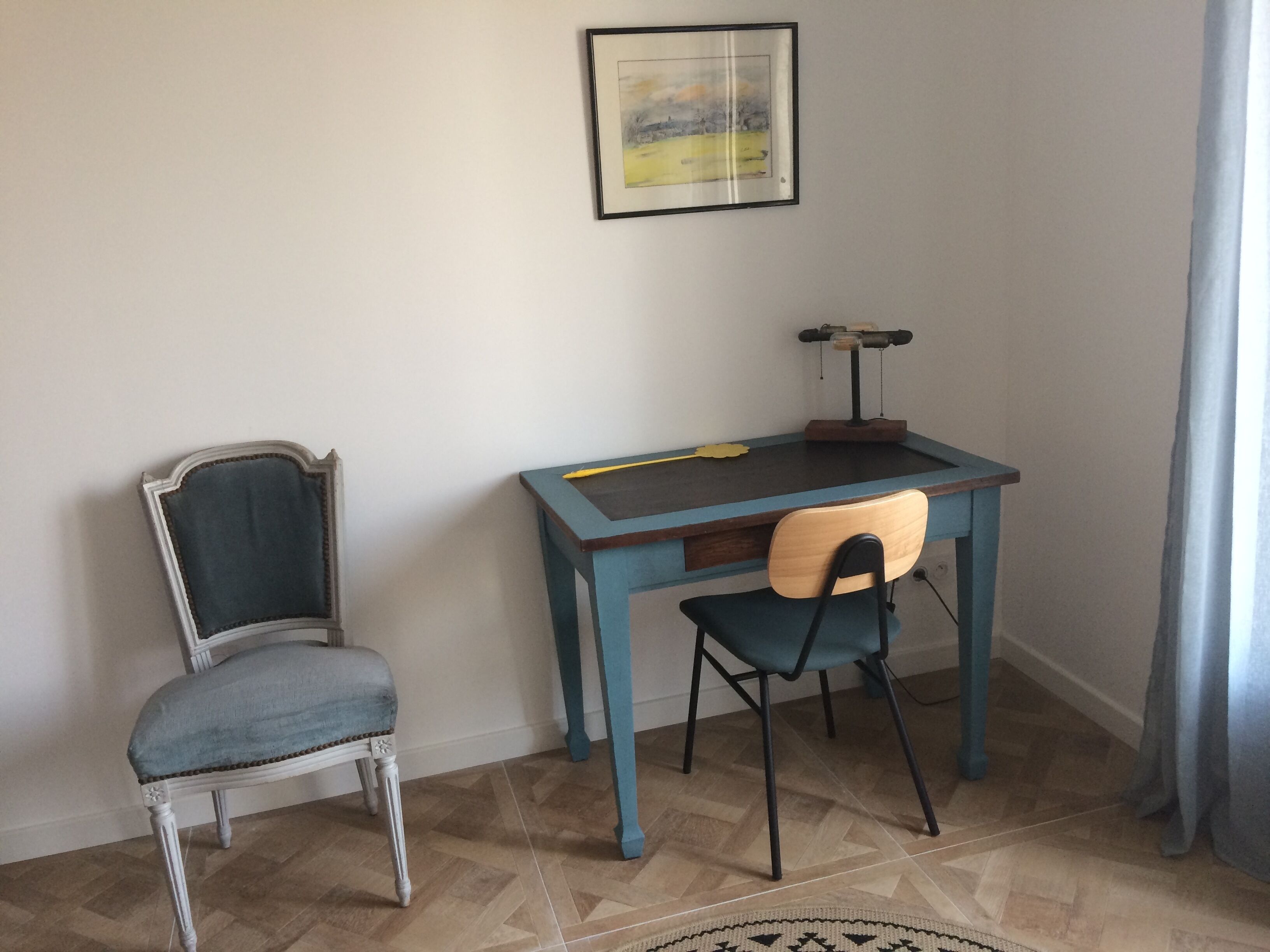 A small study room with a desk, two chairs, a framed picture on the wall, and a patterned rug on the floor.