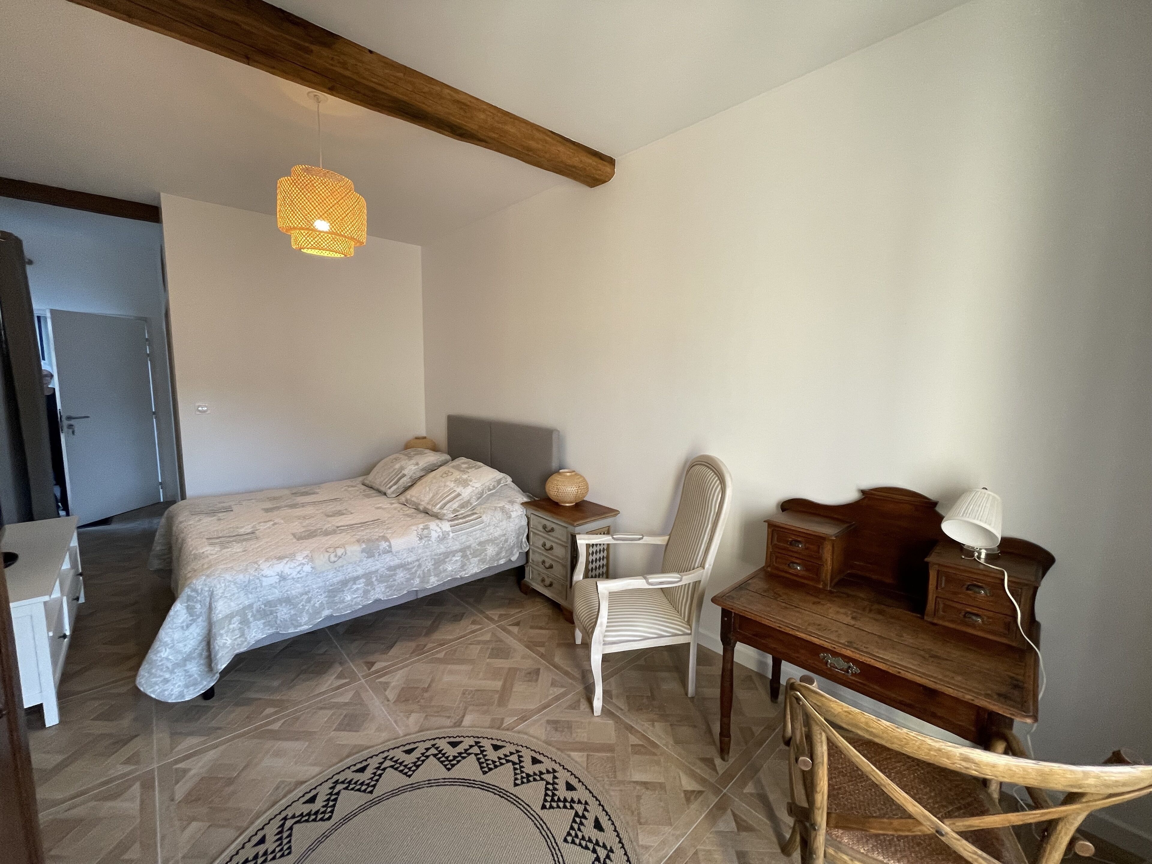 Une chambre à coucher comprenant un lit, une table de chevet, une chaise, un bureau, une lampe et un luminaire suspendu.