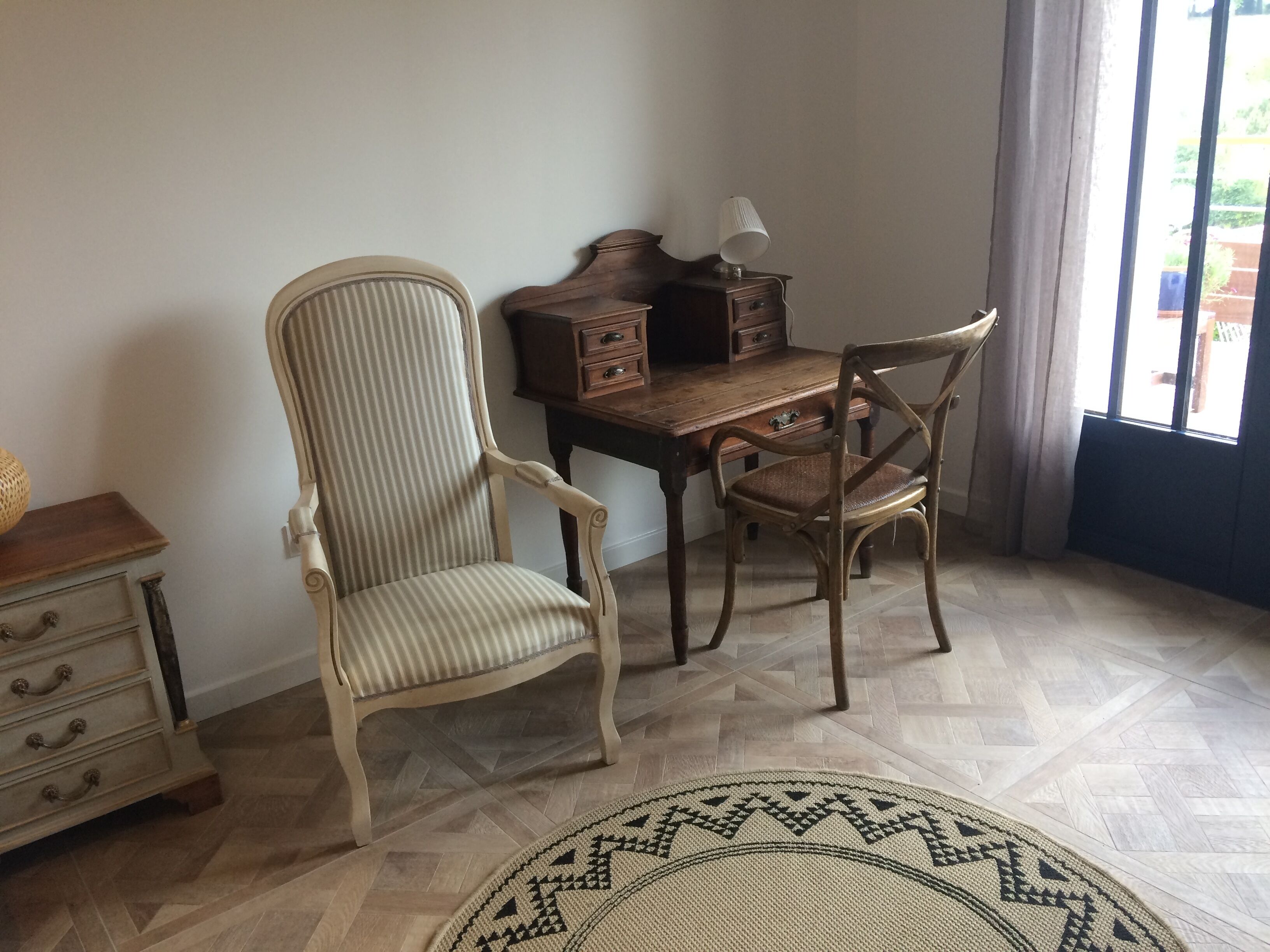 A room with a wooden desk, two chairs, a lamp, and a patterned rug.