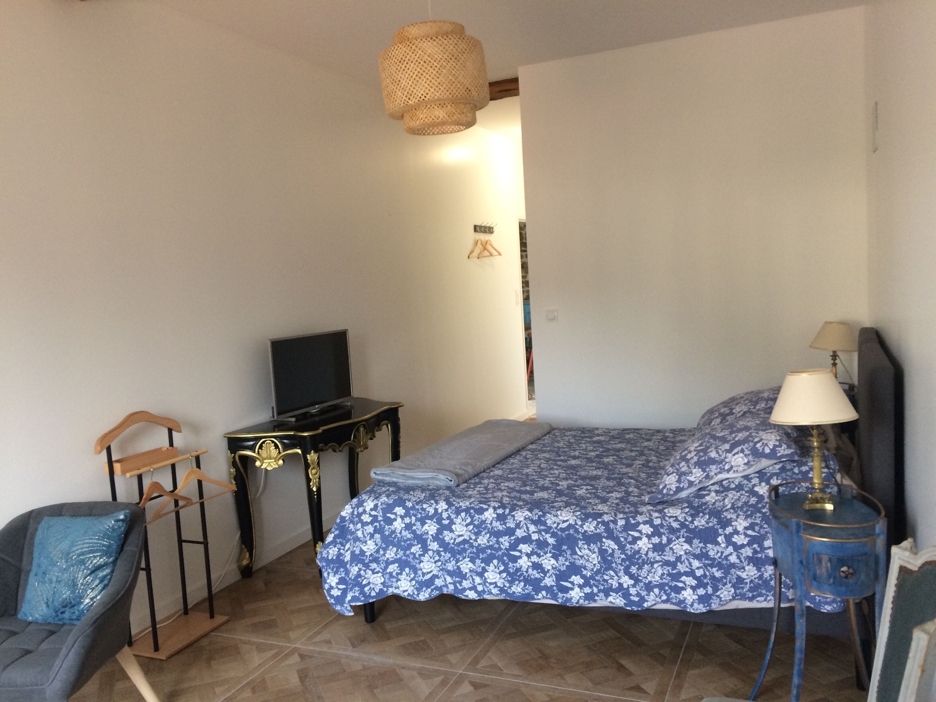 Quarto com cama, televisão, mesa de cabeceira, cadeira e luminária pendente.