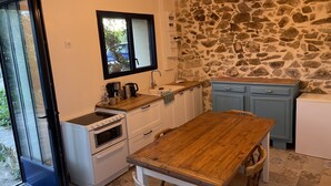 Una cocina compacta con pared de piedra, mesa de madera y muebles de cocina blancos.