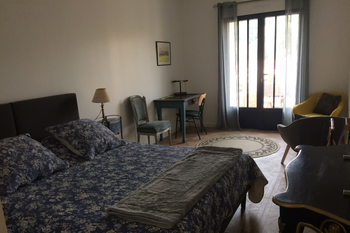 Quarto com uma cama grande, uma escrivaninha, duas cadeiras e uma janela com cortinas.