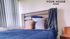 Un dormitorio con cama, almohadas, una silla y una ventana con persianas.