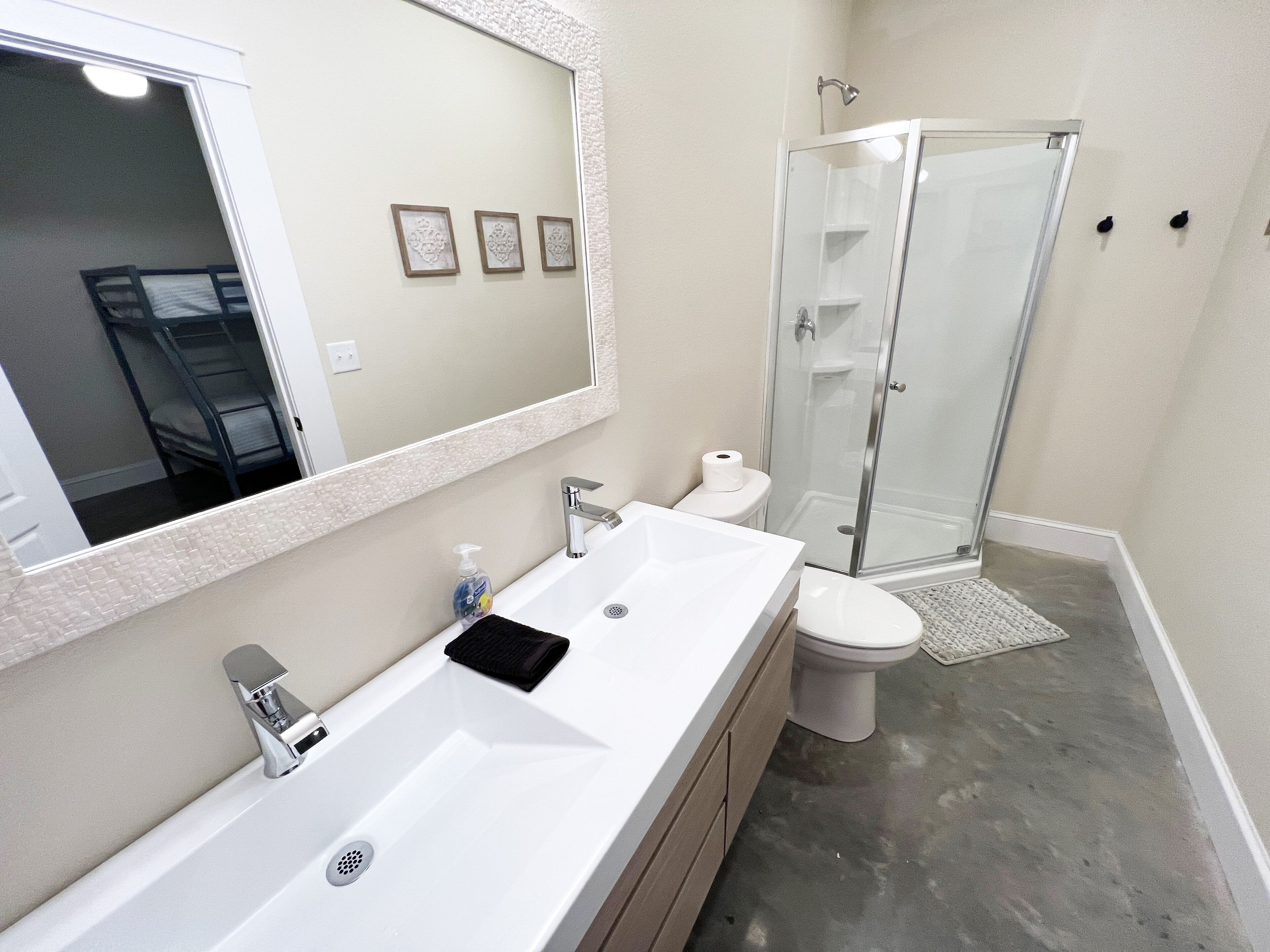 Un baño moderno con lavamanos blanco, espejo y cabina de ducha de vidrio.