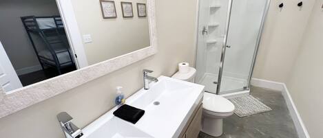 Un baño moderno con lavamanos blanco, espejo y cabina de ducha de vidrio.