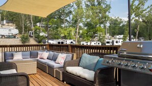 Eine überdachte Terrasse im Freien mit Korbmöbeln, einem Grill und Wohnmobilen im Hintergrund.
