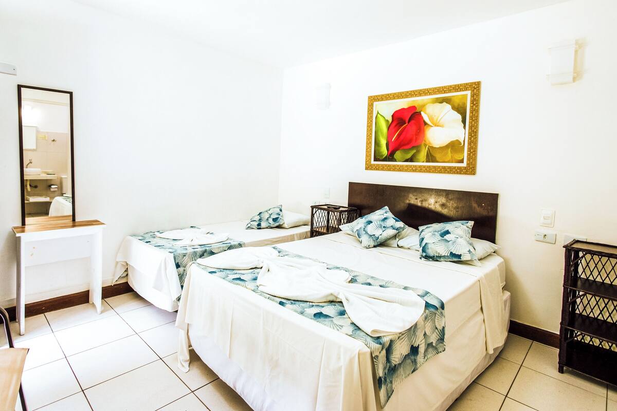Habitación de hotel con dos camas, un espejo grande, un cuadro de flores y una mesita.