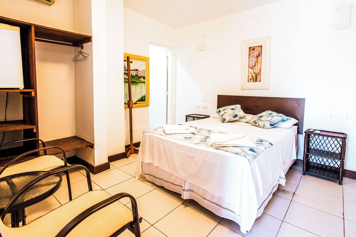 Habitación de hotel con cama, una silla, una mesita y un cuadro en la pared.