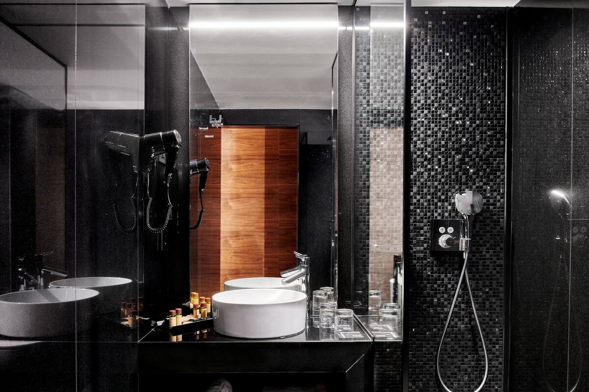A modern bathroom with two sinks, a mirror, a hairdryer, and a shower.