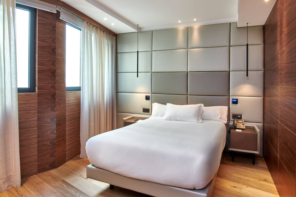 A modern hotel room with a large bed, wooden paneling on the walls, and a nightstand with a lamp and phone.