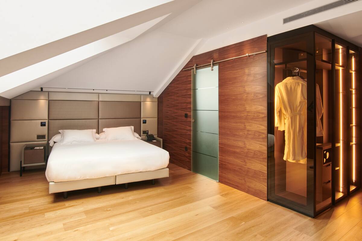 A modern bedroom with a large bed, a walk-in closet, and a sloped ceiling.