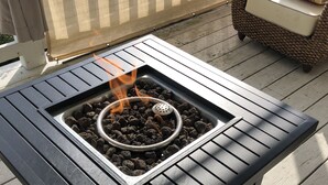 A black metal outdoor table with a built-in fire pit, surrounded by a wooden deck.