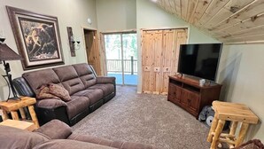 Un salon chaleureux avec un grand canapé d’angle, un téléviseur et un plafond en bois.