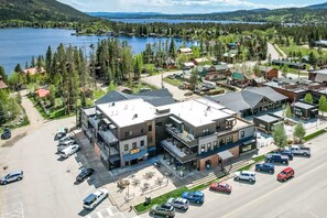 A multi-story building with a flat roof, a parking lot with several cars, and a view of a lake and forested hills in the background.