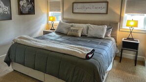 A bedroom with a bed, two bedside tables, a lamp, a framed picture, and a window with blinds. - Downtown condo short walk to lake, patio and awesome common area (Grand Lake)