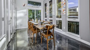 Un espace de restauration moderne, doté d’une longue table, de chaises en bois et de grandes fenêtres offrant une vue sur l’extérieur.