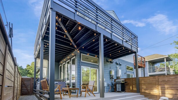 Une maison moderne dotée d’un patio couvert, d’un espace salon extérieur et d’une petite pelouse.