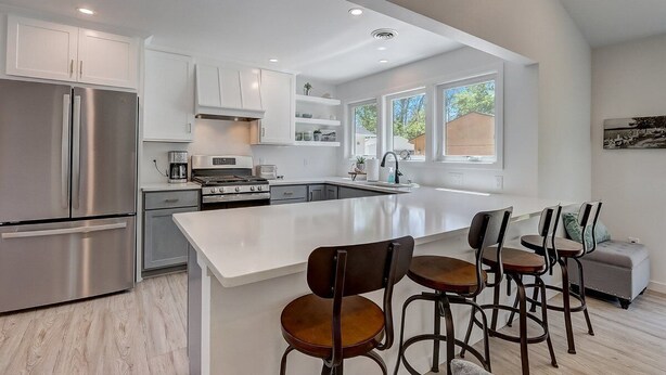 Een moderne keuken met witte kastjes, roestvrijstalen apparatuur en een groot eiland met barkrukken.