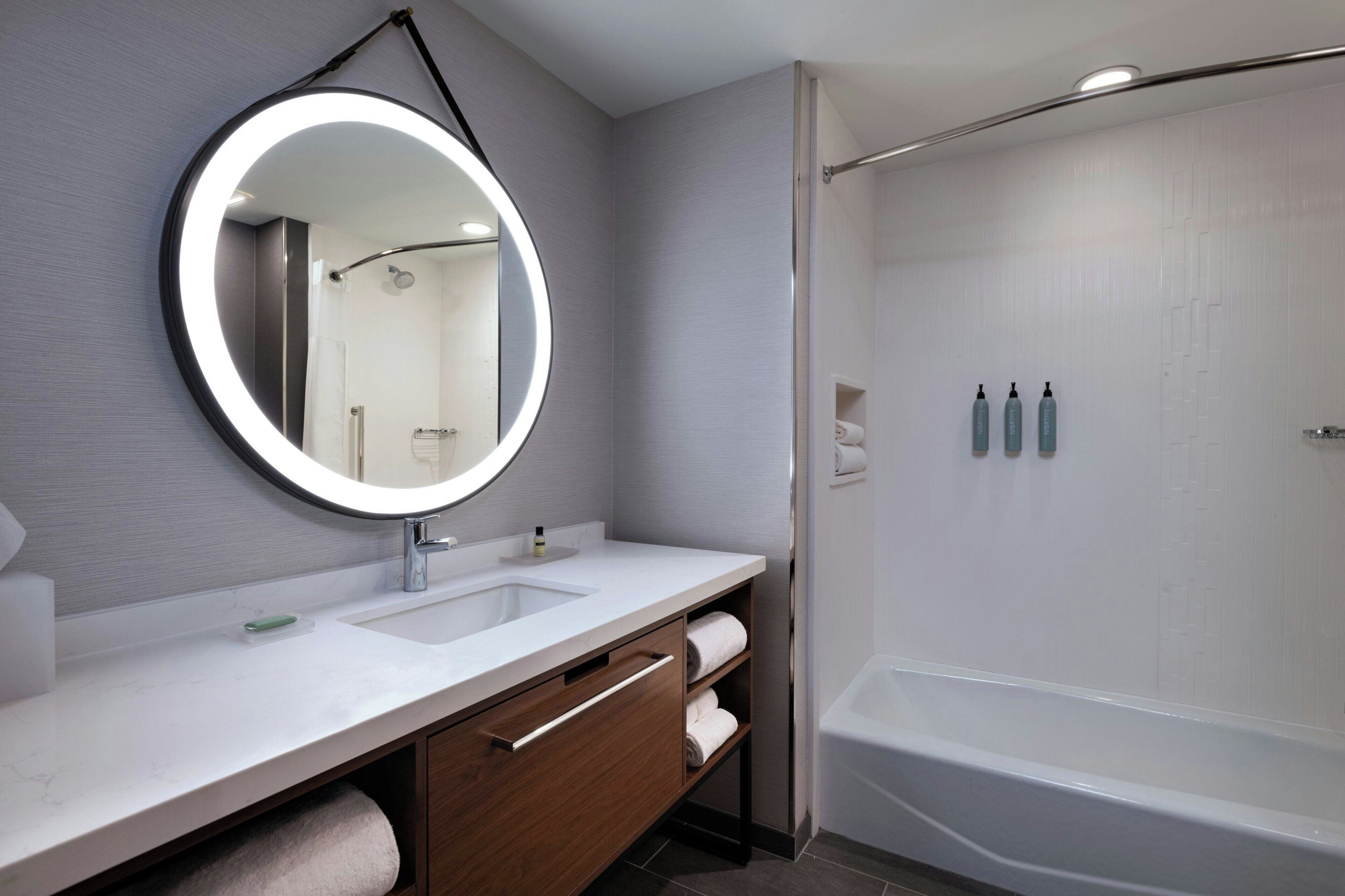 A modern bathroom with a round mirror, two sinks, a shower, and a bathtub.