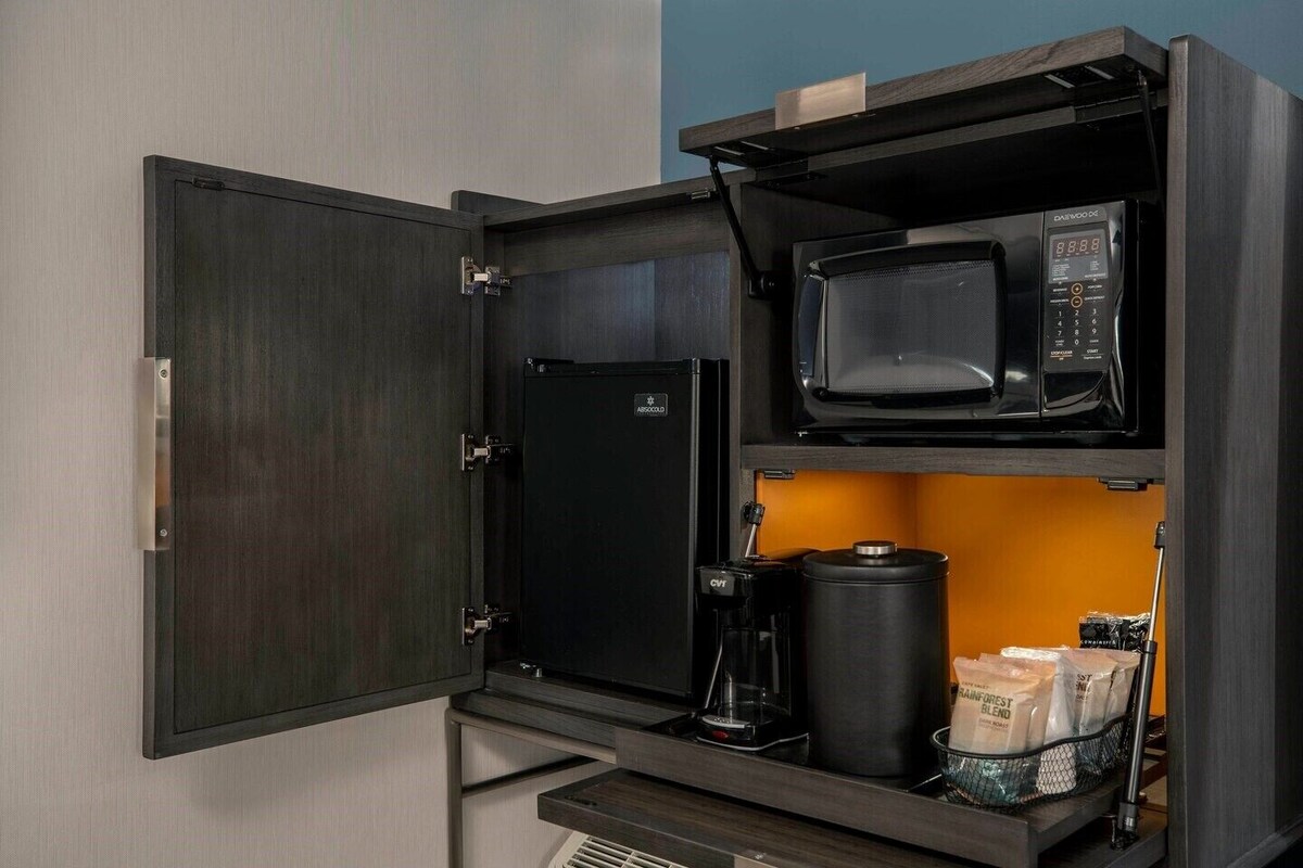 Een compact keukenhoekje met een magnetron, koffiezetapparaat en ruimte voor koffiebonen.