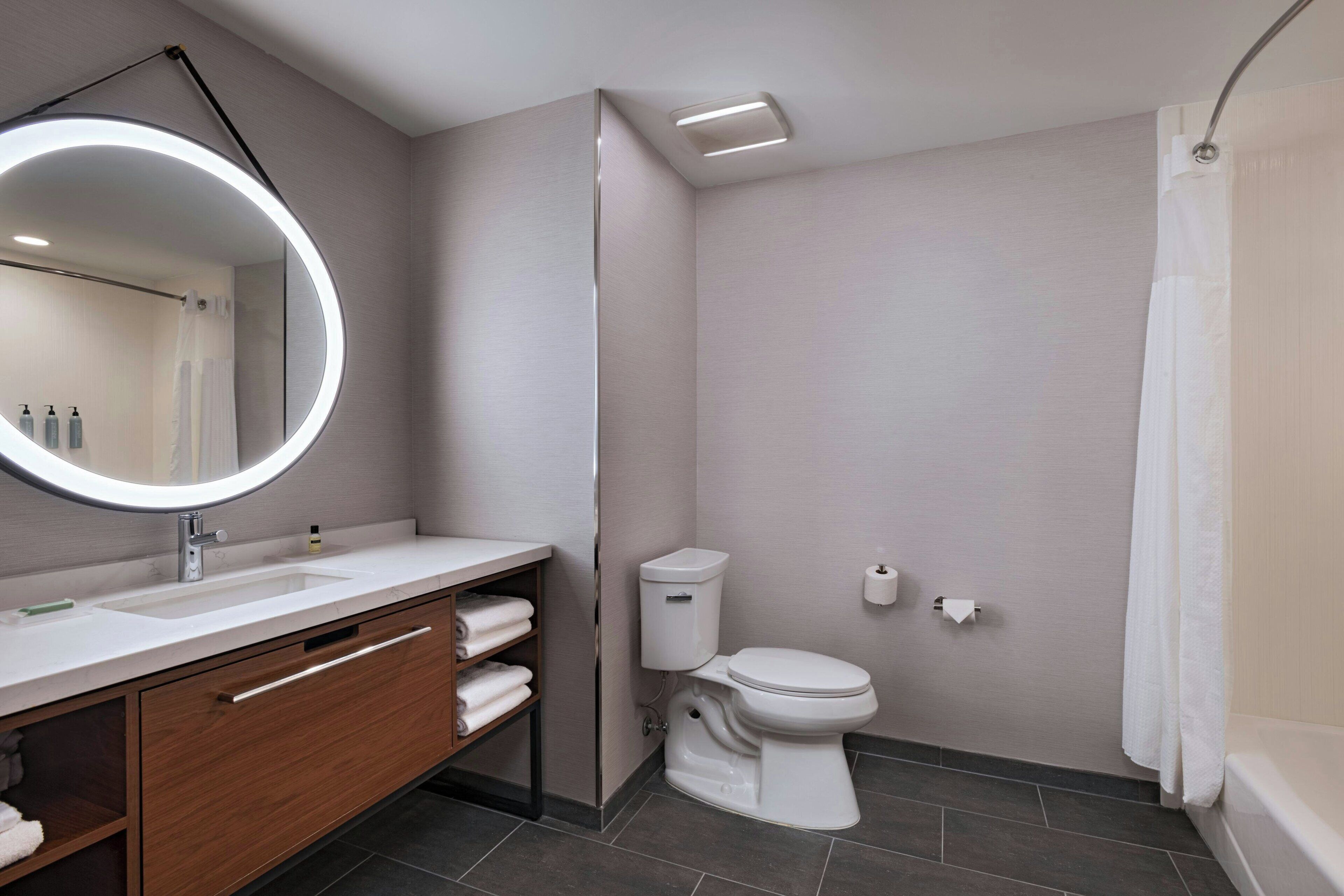 A modern bathroom with a round mirror, white sink, and toilet.
