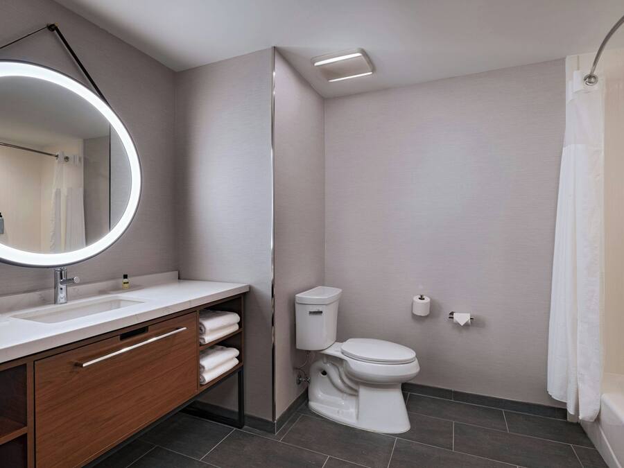 A modern bathroom with a round mirror, white sink, and toilet.
