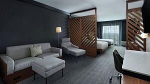 Een moderne hotelkamer met een grijze bank, een fauteuil, een bureau en een bed.