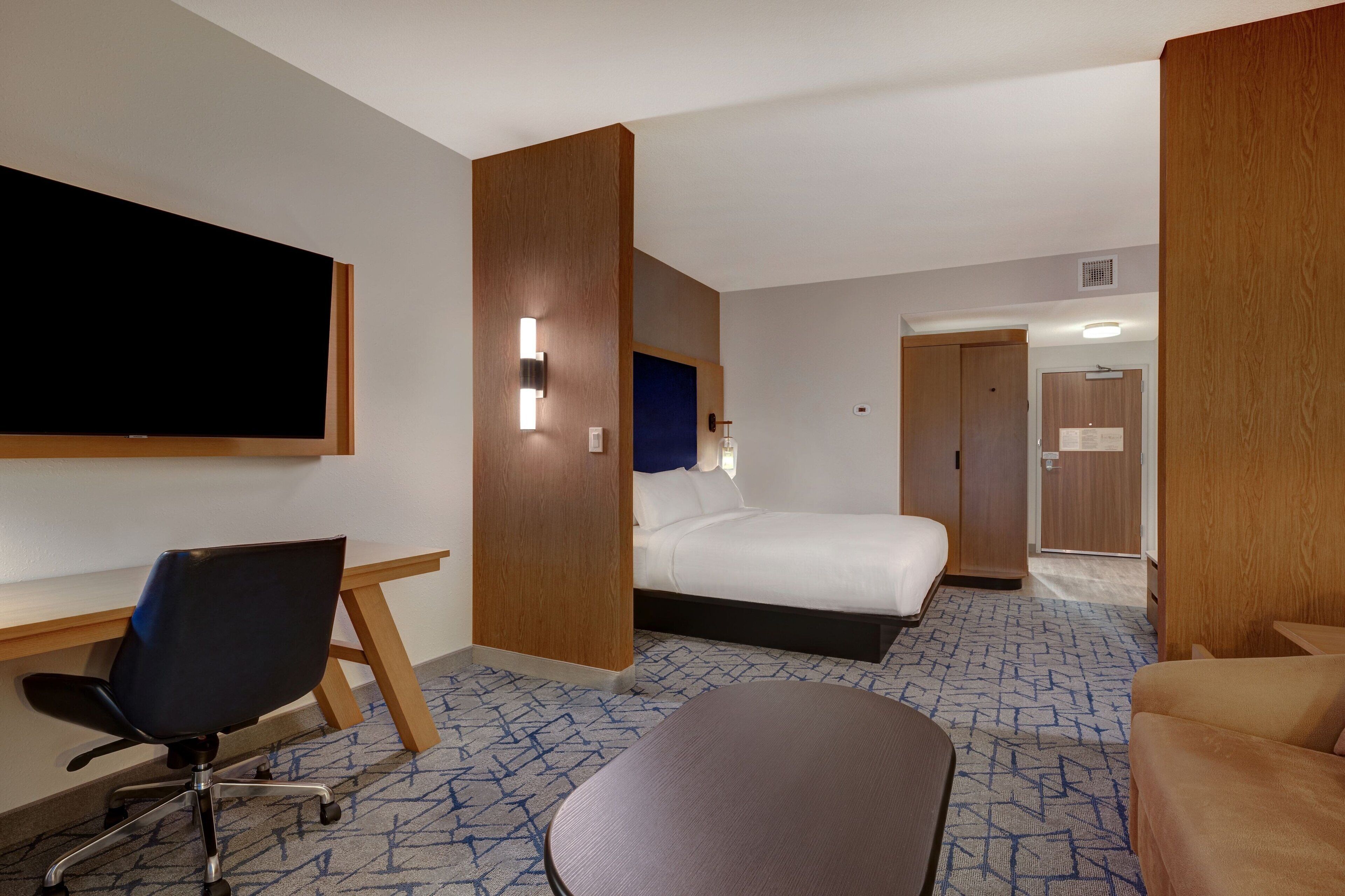 A hotel room with a bed, a desk, a chair, and a TV.