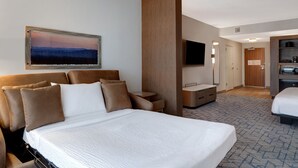 Een hotelkamer met een groot bed, een bureau, een televisie en een badkamer die door een open deur zichtbaar is.