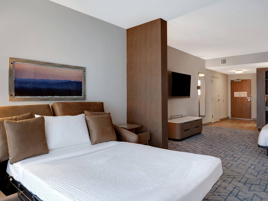 A hotel room with a large bed, a desk, a television, and a bathroom visible through an open door.