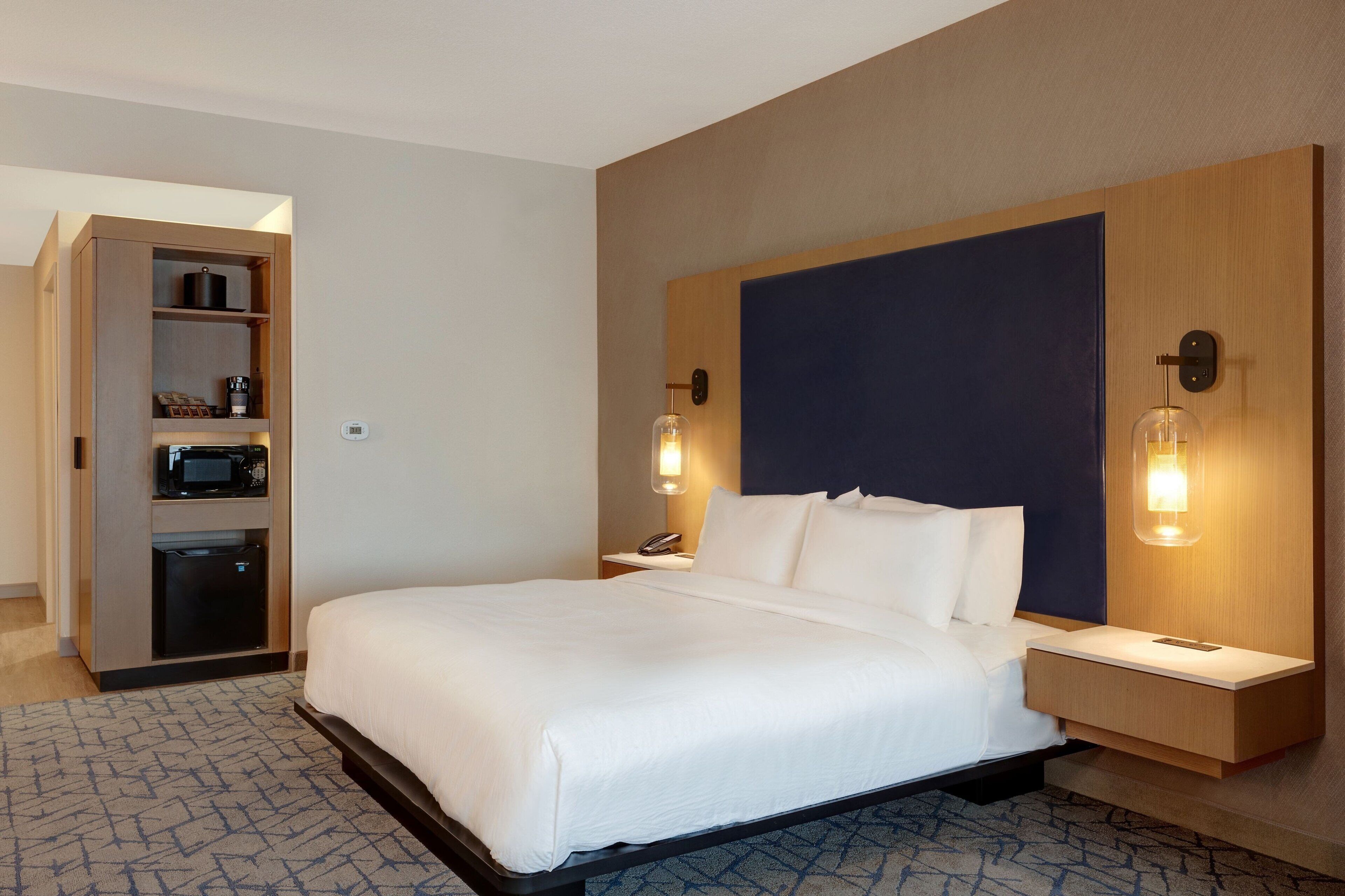Hotelkamer met een groot bed, een houten hoofdbord, nachtkastjes, een inbouwkast en een wandlamp.