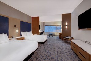 Quarto de hotel com duas camas, uma escrivaninha, uma cadeira e uma televisão.