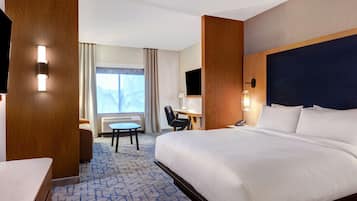 A hotel room with a large bed, a desk, a chair, and a view of the mountains through the window.