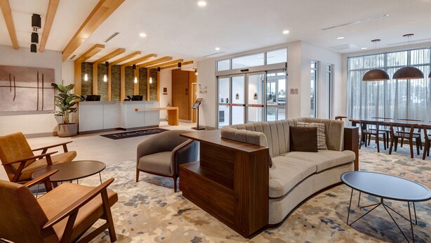 Een moderne hotelentree met een houten receptiebalie, een zithoek en grote ramen met uitzicht.