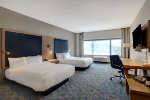 Quarto de hotel com duas camas, uma escrivaninha, uma cadeira e uma televisão.
