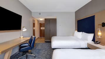 A hotel room with two beds, a desk with a chair, a desk lamp, a telephone, and a wall-mounted light fixture.