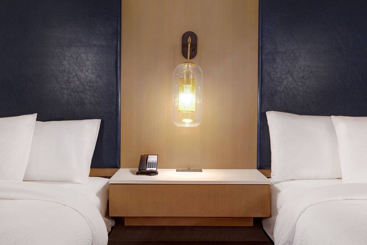 Ein Hotelzimmer mit zwei Betten, einem hölzernen Kopfteil, einem Nachttisch mit Telefon und einer wandmontierten Lampe.
