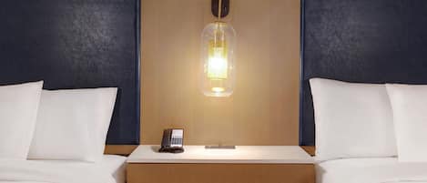 Una habitación de hotel con dos camas, cabecero de madera, mesita de noche con teléfono y lámpara de pared.