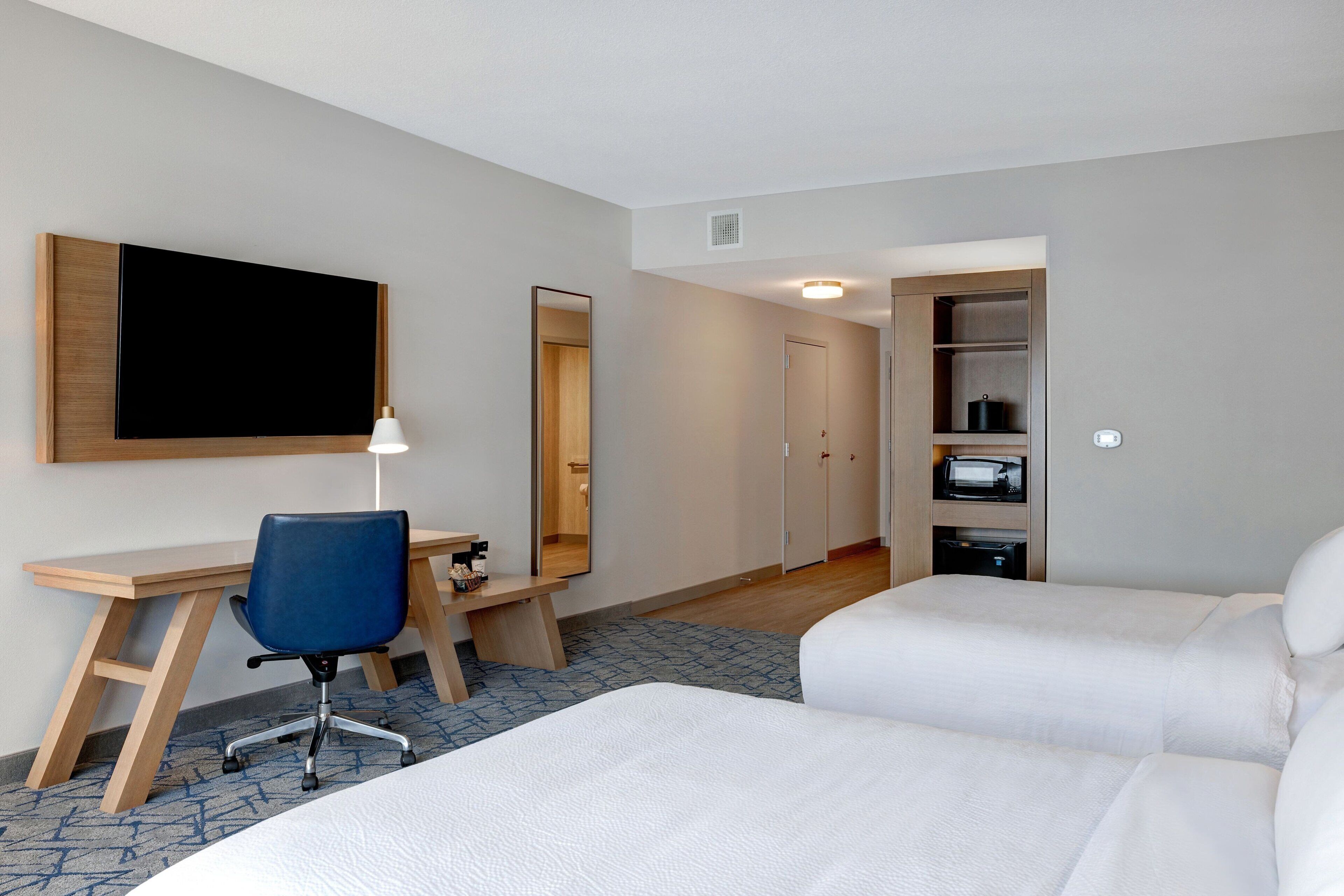 Una habitación de hotel con escritorio, silla, cama, armario y espejo.