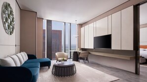 A modern living room with a sofa, a round coffee table, a TV, and a large window offering a city view. - Tianjin Marriott Hotel National Convention And Exhibition Center (Tianjin)