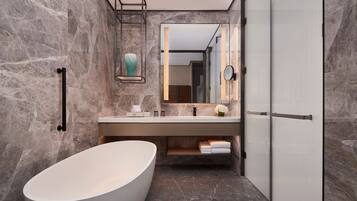 A modern bathroom with a freestanding bathtub, a marble wall, a vanity with a mirror, and a towel rack.